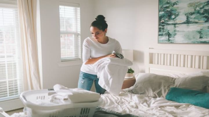 A woman folding clean laundry on her bed.