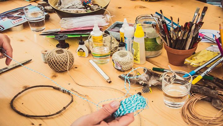 A craft table covered with string, glue, and paint brushes.