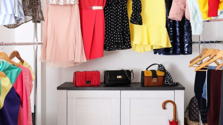 A woman's organized closet with dresses hanging above a cabinet.