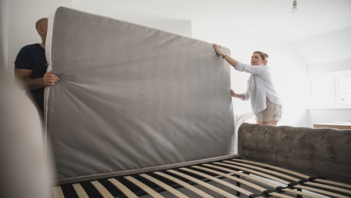 A couple putting a mattress on a bed frame.