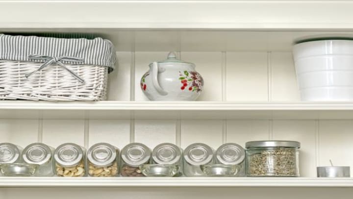 White pantry shelves lined with glass containers and a white tea pot.