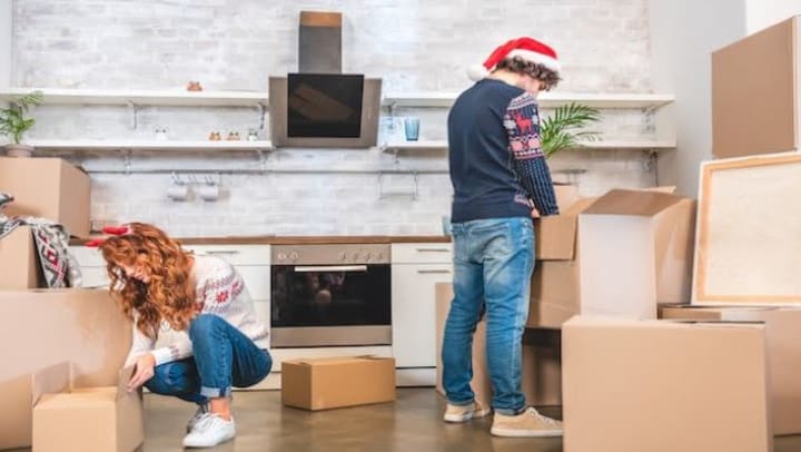 A couple in Christmas sweaters packing up their kitchen.