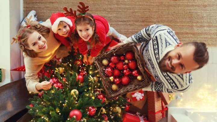 A couple and their two children decorating a Christmas tree with red and gold ornaments.