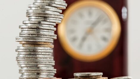 Coins stacked up on each other with a clock in the background