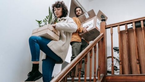 Two people carrying backing boxes of books and plants as they move out.