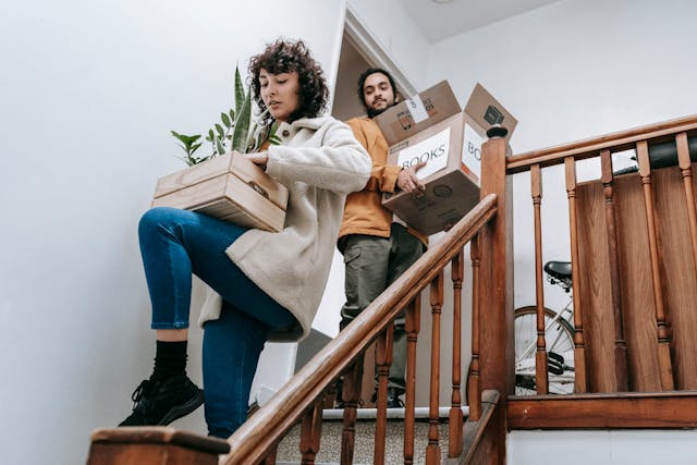 Two people carrying backing boxes of books and plants as they move out.