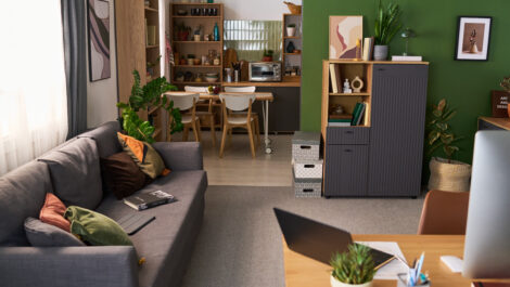 Wide angle view of modern home office and living room featuring computer workspace and dining area, illustrating remote work setup for productivity, hybrid work marketing